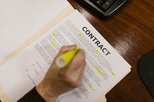 Focused view of a person highlighting text in a contract document on a wooden office desk.